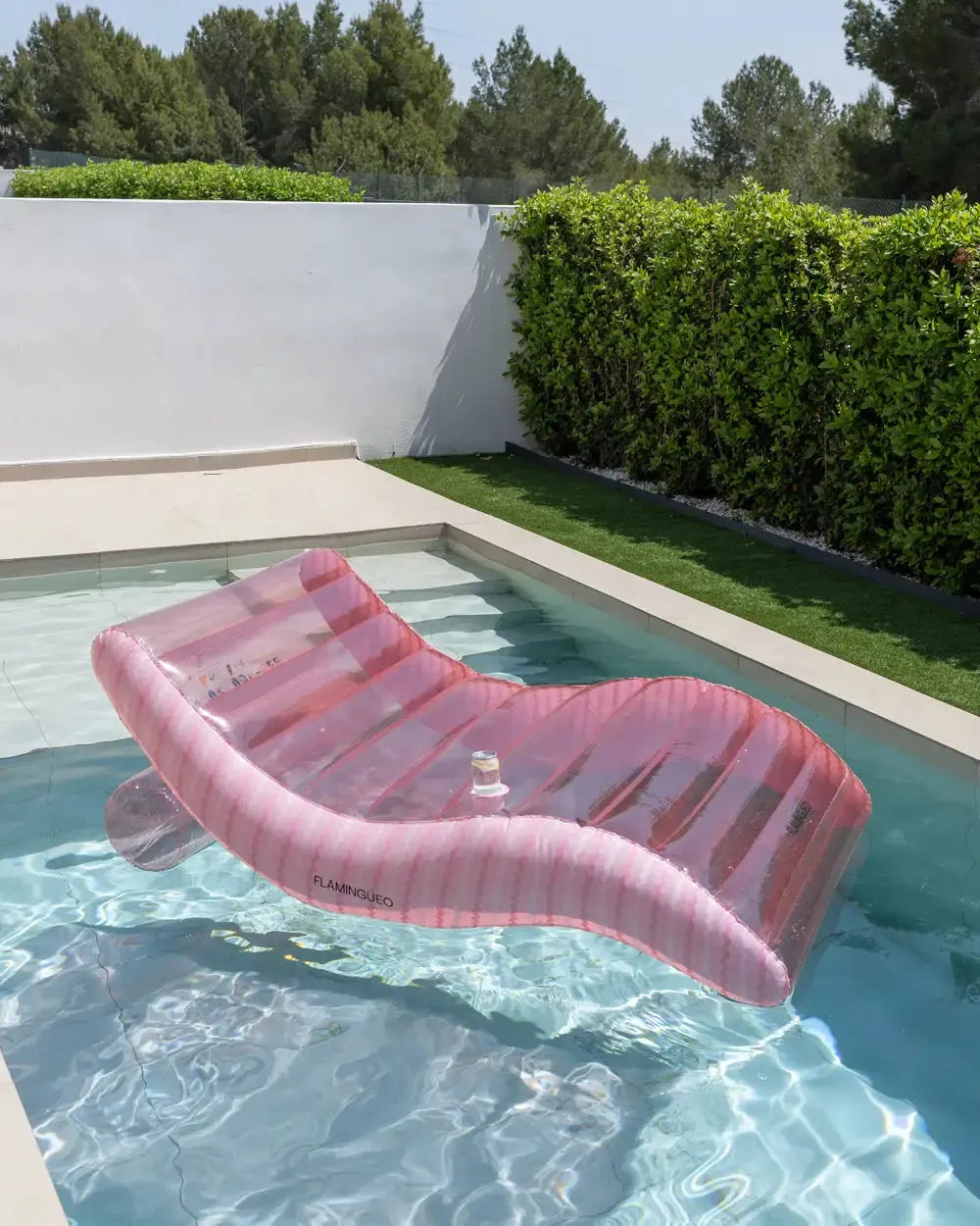 Colchão insuflável rosa a flutuar sozinho na piscina com uma bebida no porta-copos