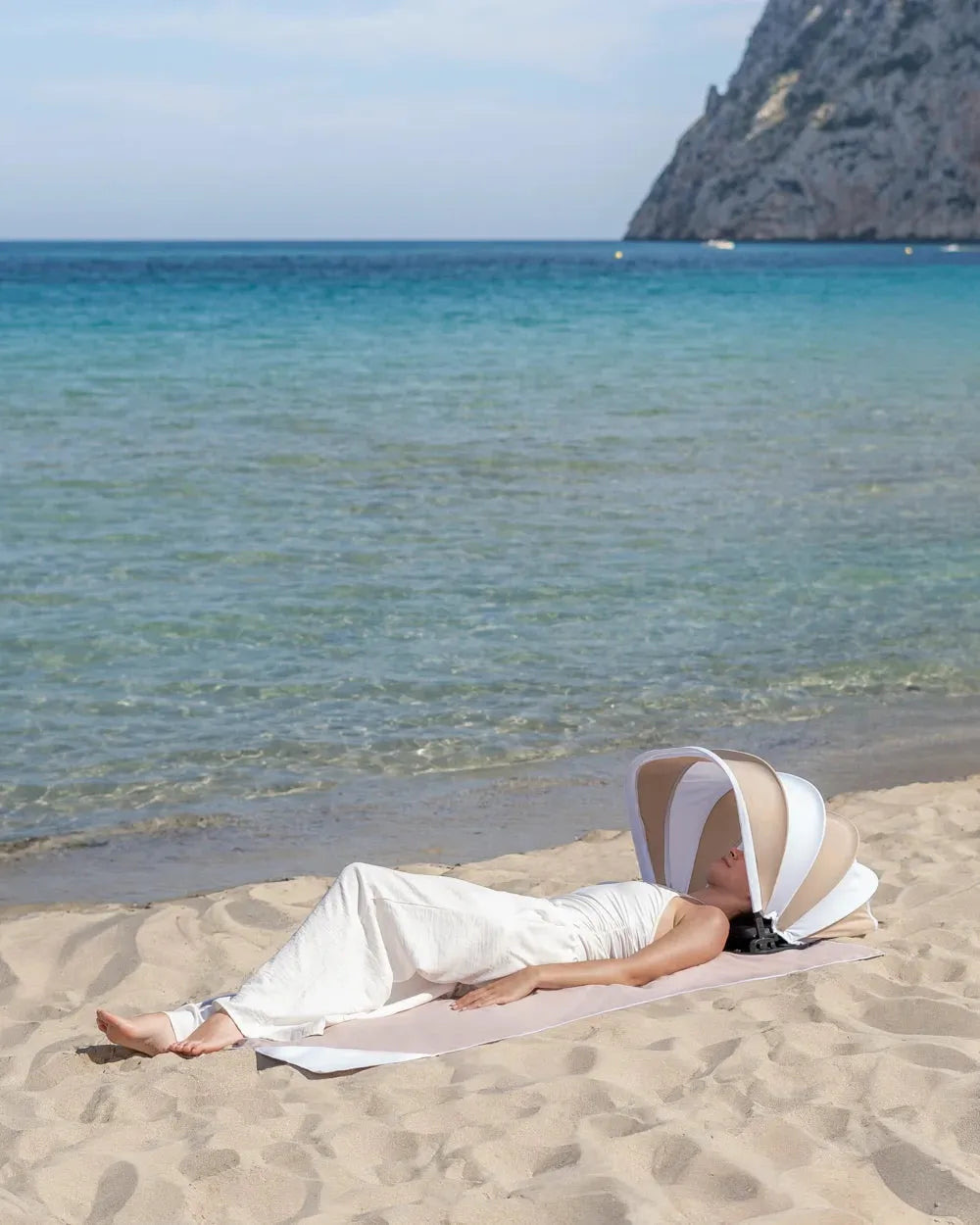 Mulher deitada na praia protegida do sol pelo toldo pessoal, com o mar e a falésia atrás