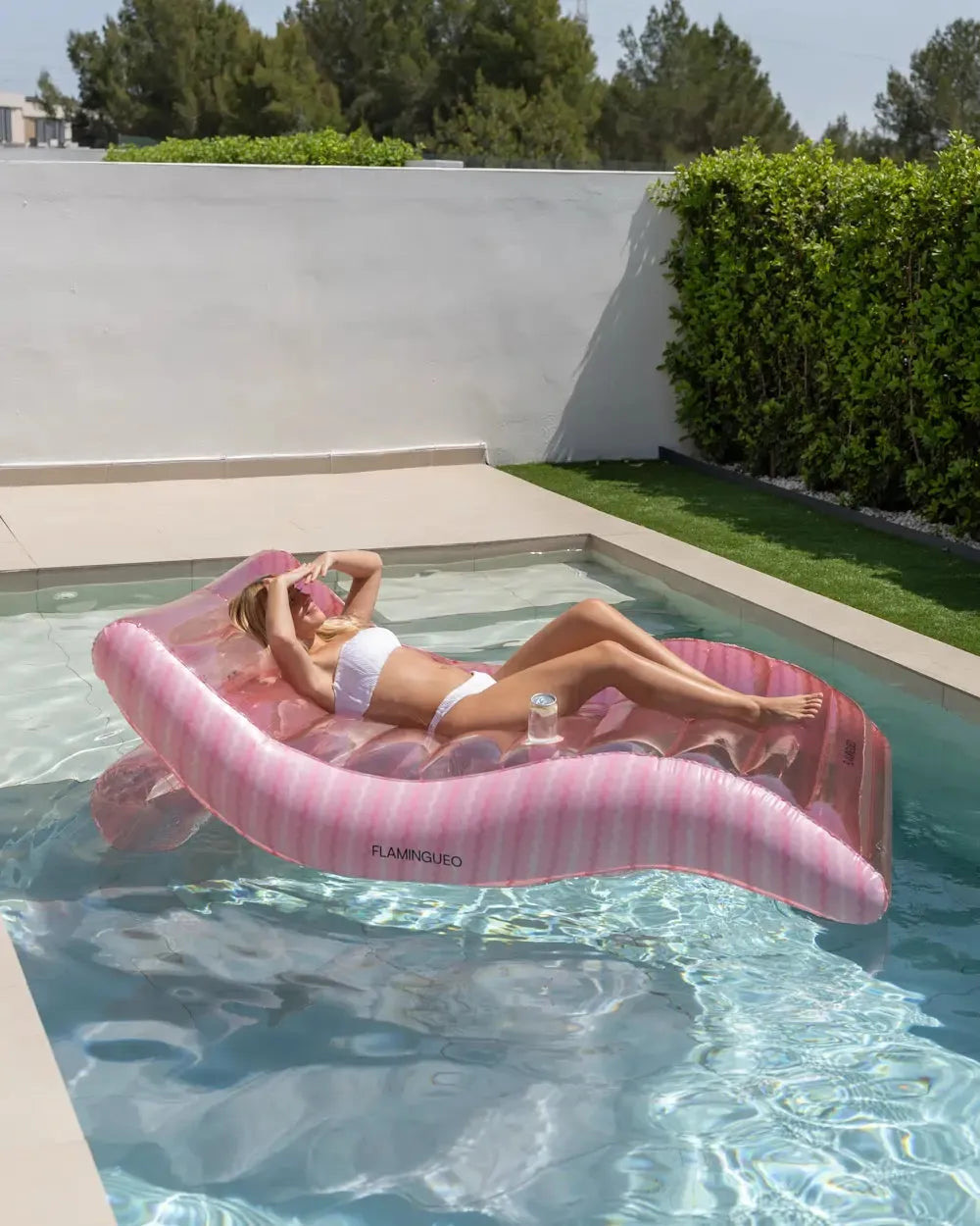 Mulher a relaxar deitada no colchão insuflável rosa dentro da piscina, com bebida no porta-copos